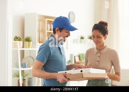 Junge Frau, die die Pizza bestellt und die Lieferung zu Hause unterzeichnet Stockfoto