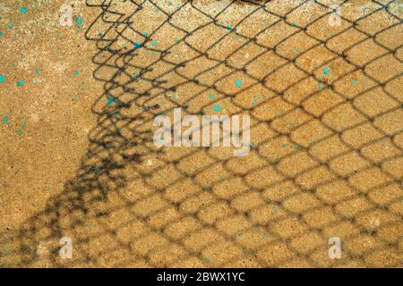 Gebrochener Kettenzaun Schatten auf Betongrund. Stockfoto