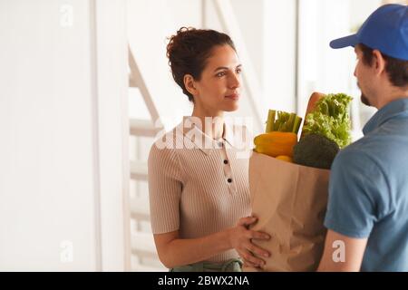 Junge Frau, die Produkte von Lieferung Mann sie Bestellung von Lebensmitteln zu Hause Stockfoto