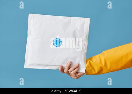 Nahaufnahme der weiblichen Hand, die ein Paket in weißem Papier verpackt hält, isoliert auf blauem Hintergrund Stockfoto