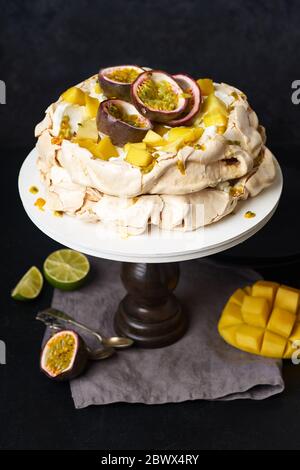 Pavlova Kuchen mit Passionsfrucht, Mango, Limette und Bananencreme auf dunklem Hintergrund Stockfoto