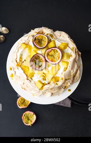 Pavlova Kuchen mit Passionsfrucht, Mango, Limette und Bananencreme auf dunklem Hintergrund Stockfoto