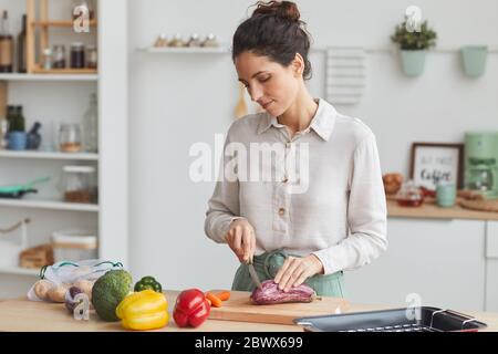 Junge Frau schneidet frisches Gemüse auf dem Schneidebrett sie bereitet das Abendessen in der Küche Stockfoto