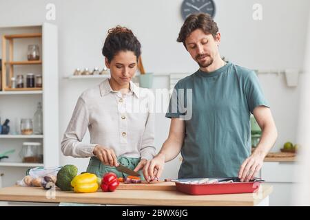 Junges Paar steht am Küchentisch und bereitet das Abendessen gemeinsam in der Küche zu Hause vor Stockfoto