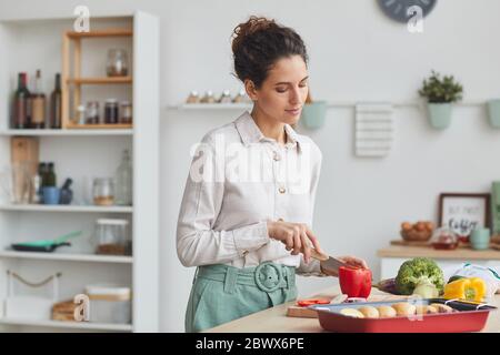 Junge Frau Schneiden roten Pfeffer auf Schneidebrett sie bereitet das Abendessen in der heimischen Küche Stockfoto
