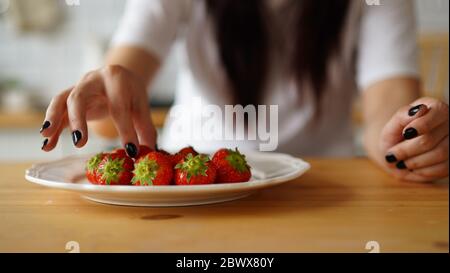 Frau, die Erdbeeren auf den Teller legt. Nahaufnahme von Frauenhänden, die frische Beeren auf den weißen Teller auf den Küchentisch legen. Stockfoto