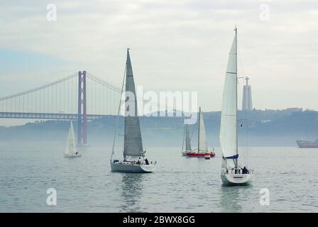 Boote auf dem Fluss Tejo mit der 25 Abril Brücke und der Cristo Rei in Lissabon, Portugal Stockfoto