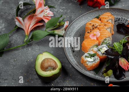 Köstliche frische Sushi-Brötchen mit Lachs und philadelphia Käse auf grauem Teller auf dunklem Steingrund. japanische Meeresfrüchte, gesundes Speisekonzept Stockfoto