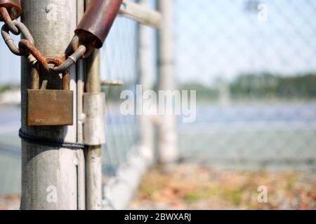 Alte Rusty Vorhängeschloss hängen an der Kette mit verschwommenem Metallzaun Hintergrund. Stockfoto