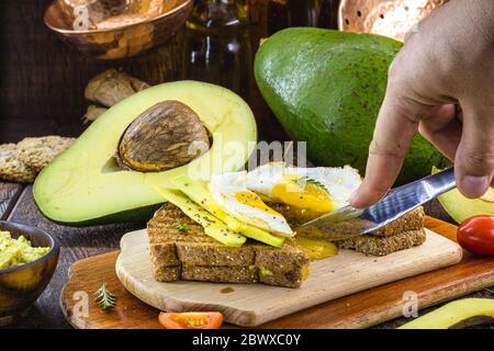Handschneidende Avocado-Toast mit gebratenem Ei in der Mitte, Eigelb tropft. Gesundes Frühstück. Stockfoto