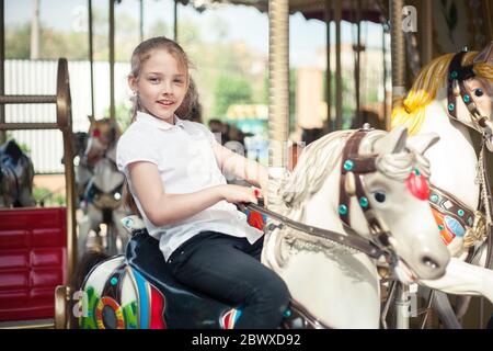 Ein Mädchen, das auf einem Karussell im Park auf einem Spielzeugpferd reitet. Stockfoto