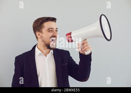 Ein Mann in einer Jacke schreit in einem Bullhorn auf grauem Hintergrund. Stockfoto