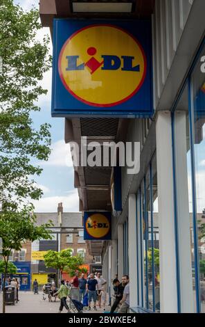 Die Schilder und Geschäfte vor einer Filiale von Lidl Supermarkt mit Menschen Schlange am Eingang, um in. Ein expandierender deutscher Discountmarkt. Stockfoto