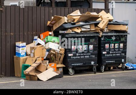 Zwei kommerzielle Abfallbehälter überlaufen mit Kartonabfall mit einem weiteren Stapel von Kisten in der Seite. Stockfoto