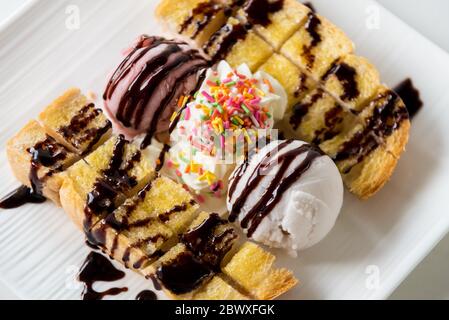 Nahaufnahme Draufsicht Honig Toast Brot serviert Vanille Kokosmilch Eis Schaufel mit Schokoladensirup dekorieren und Sahne Zucker Topping in einem Whi bestreuen Stockfoto