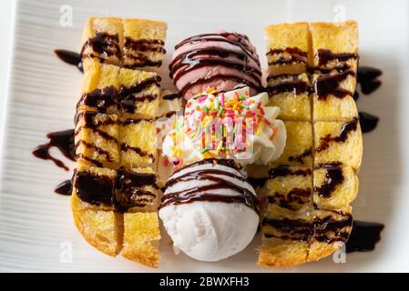 Nahaufnahme Draufsicht Honig Toast Brot serviert Vanille Kokosmilch Eis Schaufel mit Schokoladensirup dekorieren und Sahne Zucker Topping in einem Whi bestreuen Stockfoto