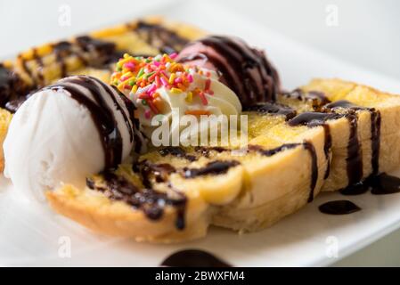 Nahaufnahme Seitenansicht Honig Toast Brot und Schokolade braun Eiscreme Schaufel mit Schokoladensirup gekrönt schmücken mit einer Schokolade Tablette in einem weißen Teller Stockfoto