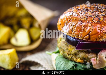 Veganer Burger ohne tierische Zutaten oder Gluten. Gemüseburger, mit Salat im Hintergrund, auf rustikalem Tisch. Vegane Gourmetküche. Stockfoto