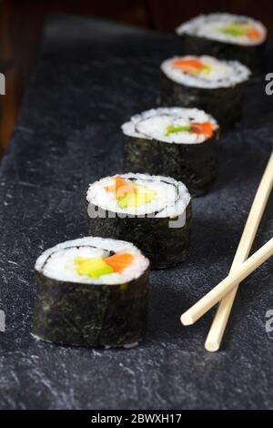 Japanische Küche. Hausgemachte Lachs-Sushi-Rolle mit Avocado und Gurke auf einem dunklen Steinteller. Nahaufnahme. Selektiver Fokus Stockfoto