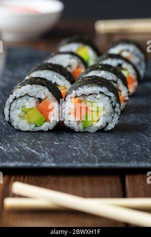 Japanische Küche. Hausgemachte Lachs-Sushi-Rolle mit Avocado und Gurke auf einem dunklen Steinteller. Nahaufnahme. Selektiver Fokus Stockfoto