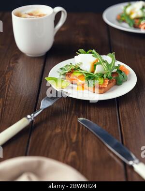 Frühstück mit Kaffee und Toast mit Avocado, Lachs Fisch, pochiertes Ei, Rucola Salate auf einem weißen Teller. Gesundes vegetarisches Gericht Stockfoto