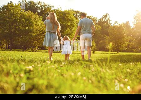 Fröhliche Familienspaziergänge auf dem Gras im Sommerpark. Mutter Vater und Kinder, die in der Natur spielen. Kinderschutztag. Stockfoto