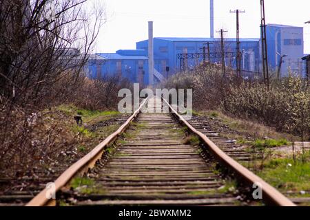 Gerade Eisenbahnstrecke, die zu alten blauen Fabrik in einem verlassenen und verschmutzten Industriegebiet geht Stockfoto