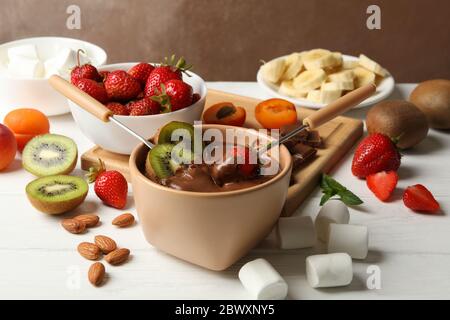 Zusammensetzung mit Zutaten für Schokoladenfondue auf weißem Holzhintergrund. Fondue wird zubereitet Stockfoto