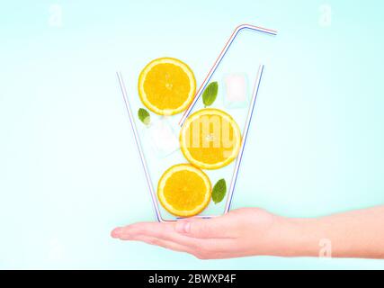 Kreatives Cocktail-Konzept für den Sommer. Glas Limonade aus Strohhalmen, Orangenscheiben, frischen Minzblättern und Eiswürfeln, die auf der Handfläche einer Frau stehen Stockfoto