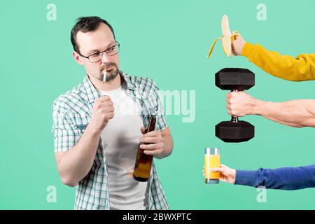 Ein Mann zündet eine Zigarette an mit einer Flasche Bier in der Hand, und zu dieser Zeit wird ihm gesundes Essen und Sport angeboten Stockfoto