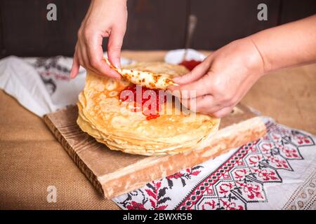 Frau wickelt roten Kaviar in einem heißen Pfannkuchen in der Küche, Hände Nahaufnahme. Stockfoto