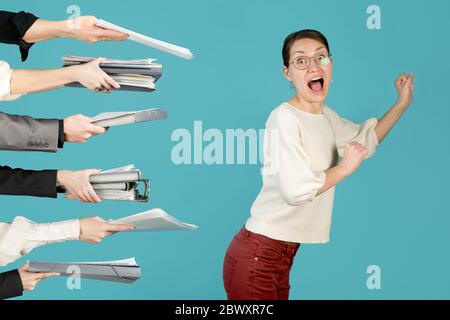 Ein Mädchen läuft von einer Menge Arbeit, die von Händen gehalten wird. Büroangestellter versucht, einer schweren Last bei der Arbeit zu entkommen Stockfoto