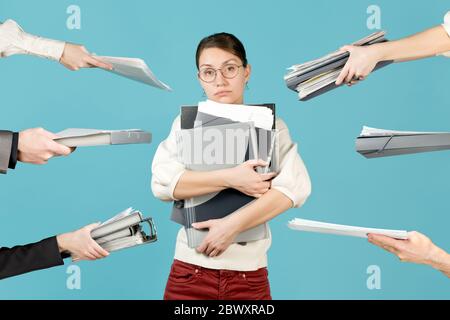 Ein trauriges Mädchen hält ein Bündel Dokumente in ihren Armen, die Hände der Mitarbeiter halten ihr weitere Ordner und Dokumente Stockfoto