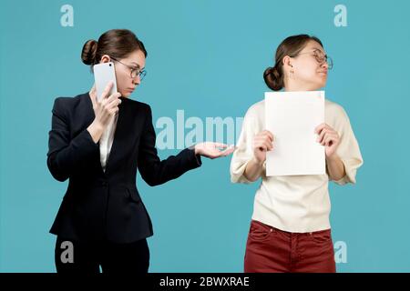 Junge verärgerte Frau mit Dokumenten in den Händen wendet sich von ihrem Chef ab, blauer Hintergrund. Beide Frauen sind ein Gesicht Stockfoto