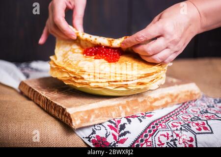 Frau wickelt roten Kaviar in einem heißen Pfannkuchen in der Küche, Hände Nahaufnahme. Stockfoto