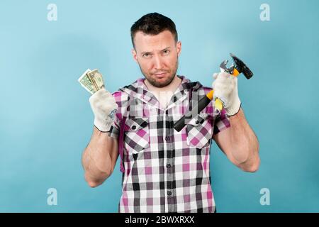 Ein schmutziger harter Arbeiter hält Werkzeuge in der einen Hand und mehrere zusammengeknitterte Dollar in der anderen. Er arbeitete hart, wurde schmutzig und müde, aber erhielt sehr wenig f Stockfoto