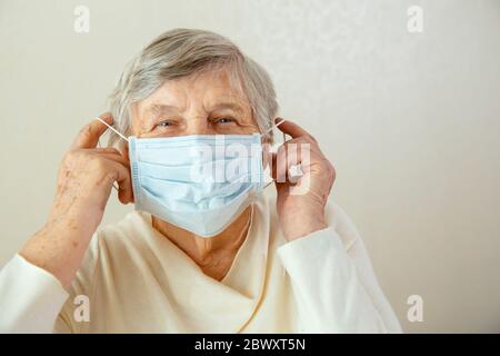 Eine ältere Frau legt ihr eine medizinische Maske ins Gesicht. Frau mit medizinischer Maske sorgt sich um Coronavirus Stockfoto