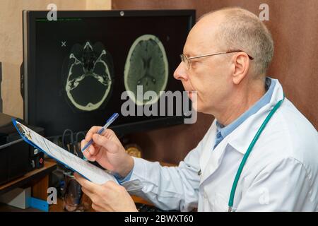 Der Arzt untersucht die Ergebnisse einer MRT-Untersuchung und zeichnet in der Krankengeschichte auf. Stockfoto