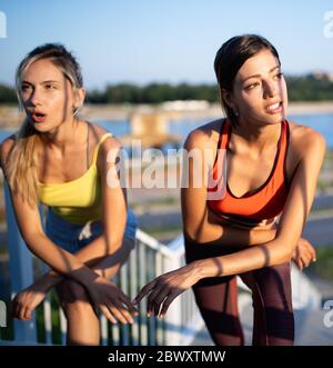 Schöne Frauen in Sportbekleidung Trinkwasser, sprechen und ruhen nach dem Training im Freien Stockfoto