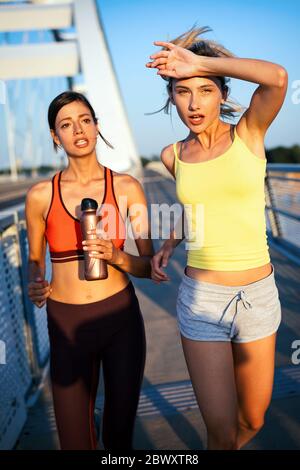 Schöne Frauen in Sportbekleidung Trinkwasser, sprechen und ruhen nach dem Training im Freien Stockfoto