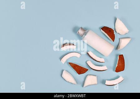 Kokosnussscheiben und Flasche gefüllt mit Kokosöl für die Lebensmittelvorbehandlung und kosmetische Schönheitsprodukte auf blauem Hintergrund mit Kopierfläche Stockfoto