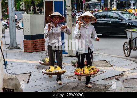 Vietnamesische Frauen mit Trageröcken Bananen zum Verkauf zu transportieren, Hanoi Stockfoto