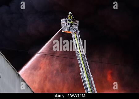 Diez, Deutschland. Juni 2020. Ein Feuerwehrmann löscht einen Großbrand von einer Drehleiter. In einem Gewerbegebiet im Rhein-Lahn-Kreis bricht in einem Unternehmen im Industriepark, das Papierrohstoffe verarbeitet, ein Brand aus. Kredit: Hasan Bratic/dpa/Alamy Live News Stockfoto