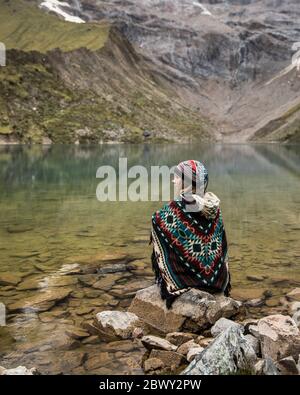 Schöne blonde Frau sitzt an einem blauen See in der Mitte der Berge in Peru. Türkisfarbener See. Stockfoto