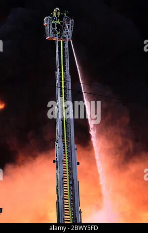 Diez, Deutschland. Juni 2020. Ein Feuerwehrmann löscht einen Großbrand von einer Drehleiter. In einem Gewerbegebiet im Rhein-Lahn-Kreis bricht in einem Unternehmen im Industriepark, das Papierrohstoffe verarbeitet, ein Brand aus. Kredit: Hasan Bratic/dpa/Alamy Live News Stockfoto