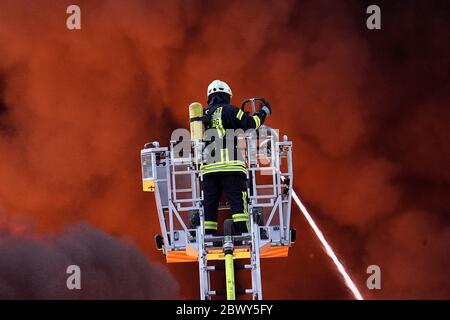 Diez, Deutschland. Juni 2020. Ein Feuerwehrmann löscht einen Großbrand von einer Drehleiter. In einem Gewerbegebiet im Rhein-Lahn-Kreis bricht in einem Unternehmen im Industriepark, das Papierrohstoffe verarbeitet, ein Brand aus. Kredit: Hasan Bratic/dpa/Alamy Live News Stockfoto