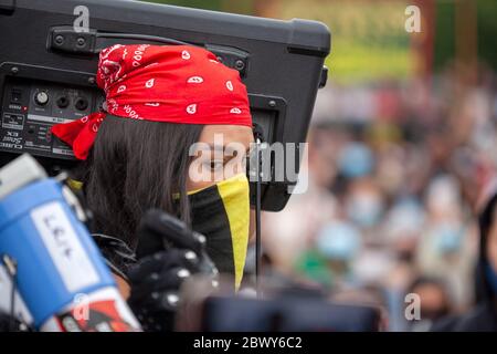 Junge Frau, die während des protestmarsches von Black Lives Matter UK einen schützenden Gesichtsschal und ein rotes Bandana trägt und einen Amp hochhält. London, England, Großbritannien Stockfoto