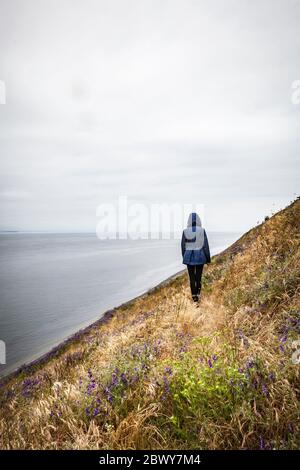 Eine eineinstehende Kapuzenfigur / junge Frau auf Ebby Bluff, Ebey's Landing National Historical Reserve, Whidbey Island, Washington, USA. Stockfoto