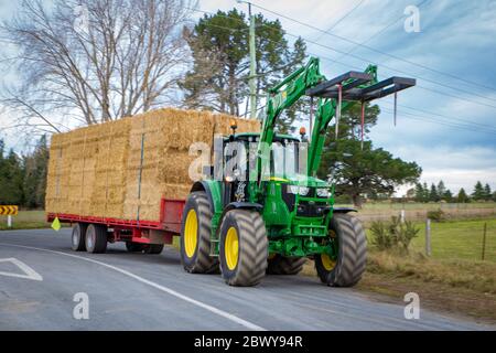 Arundel, Canterbury, Neuseeland, 3. Juni 2020: Ein Traktor auf dem Bauernhof verschiebt im Winter eine Anhängerladung Strohballen entlang einer Landstraße für die Futtermittelzuführung Stockfoto