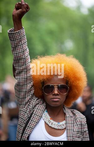 Junge Frau, mit einer orangefarbenen Afro-Frisur und Sonnenbrille, hebt stolz ihre Faust während des protestmarsches von Black Lives Matter. London, Großbritannien Stockfoto